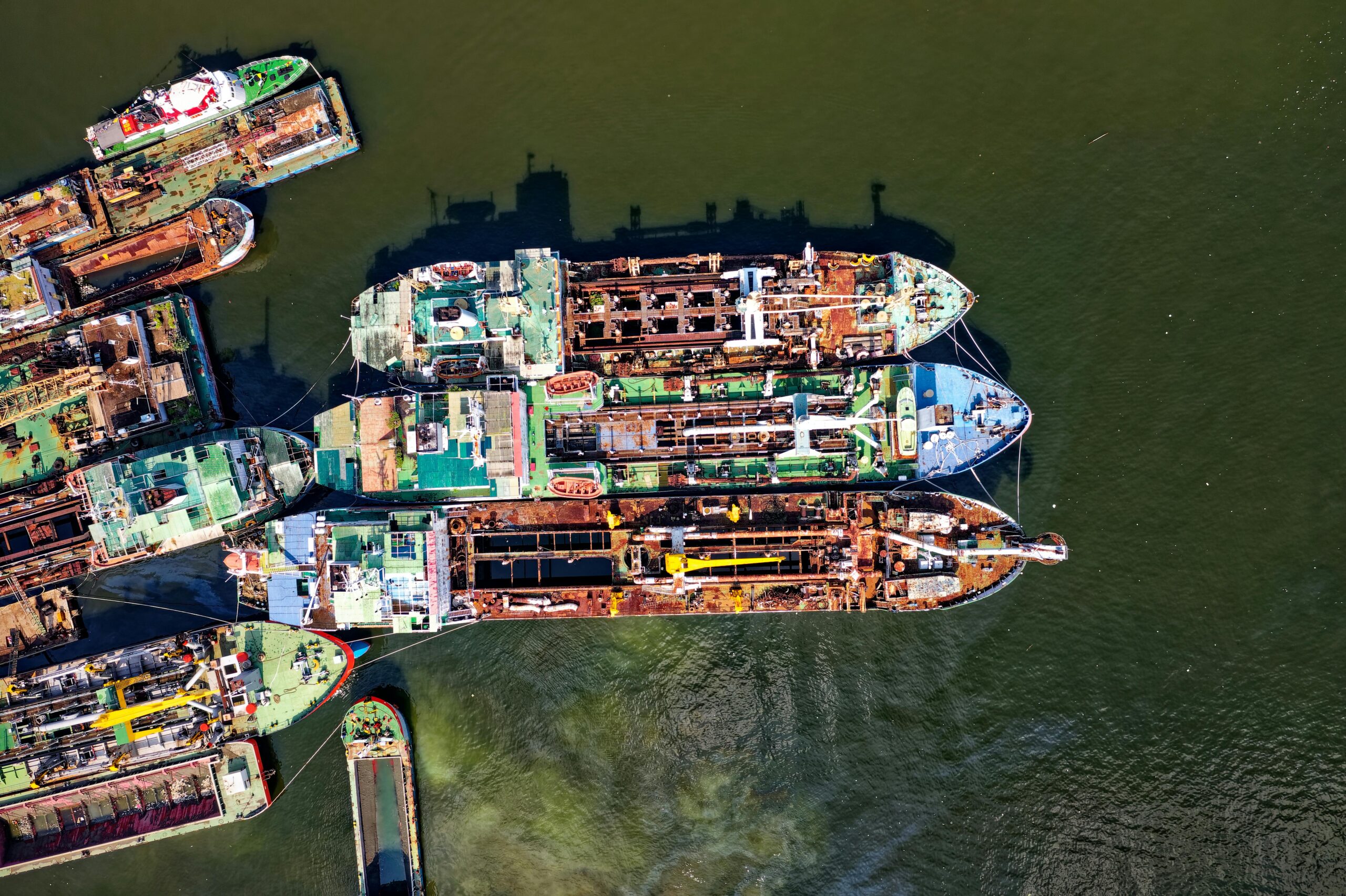 Drone shot capturing several rusted ships docked in a harbor, showcasing industrial decay.
